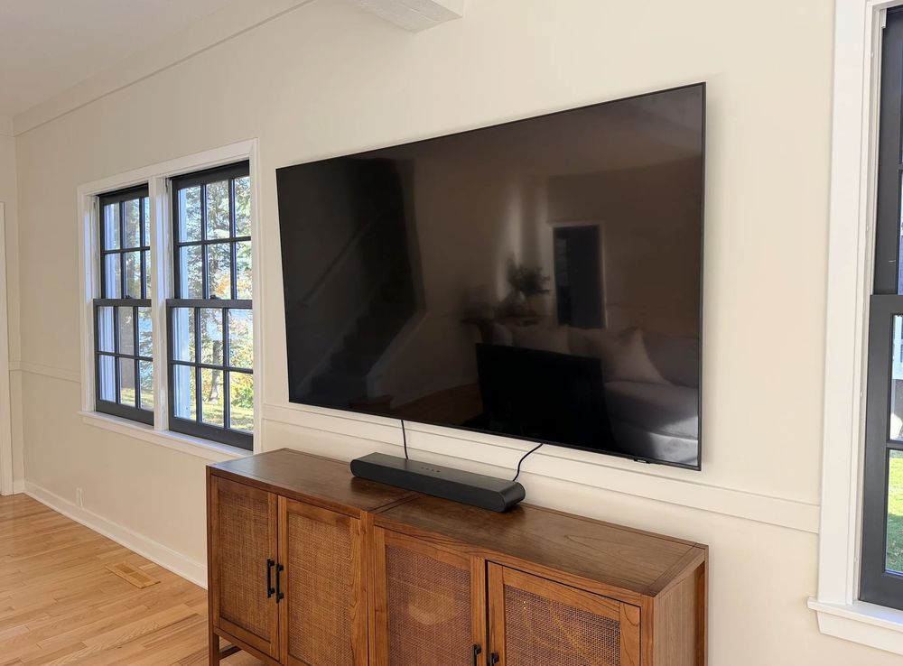 75-inch TV wall-mounted between two windows above a wooden cabinet, soundbar below, Halifax