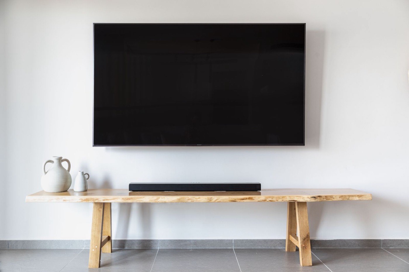 75-inch TV mounted on a plain white wall with a soundbar on the bench below and no visible wires